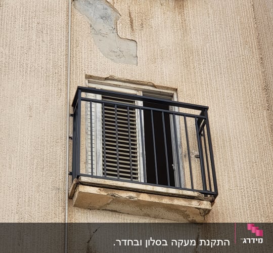 חלון עם תריסים ומעקה מתכת על קיר בניין